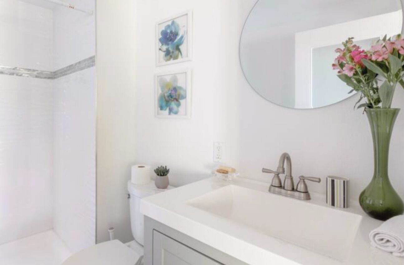 A modern bathroom with a white sink, a round mirror, and two framed floral artworks on the wall.