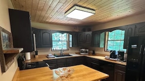A kitchen with wooden cabinets, a central island with chairs, a refrigerator, and a window providing natural light.