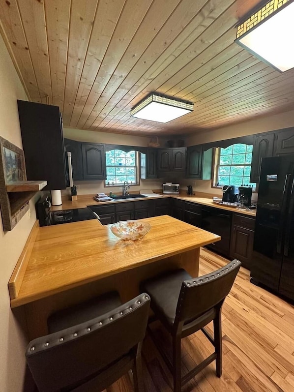 A kitchen with wooden cabinets, a central island with chairs, a refrigerator, and a window providing natural light.