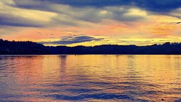 Un lac paisible au coucher du soleil, avec en arrière-plan la silhouette d’une colline boisée.