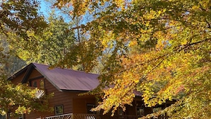 A rustic cabin with a stone foundation, wooden deck, and a metal roof.