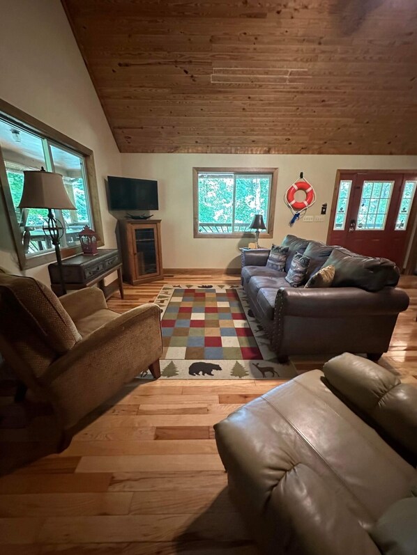 A cozy living room with a brown leather sofa, a patterned rug, and a television on a wooden stand.