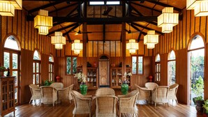A spacious room with wooden floors, wicker furniture, and large windows. - Inle Heritage Stilt House (Nyaungshwe)