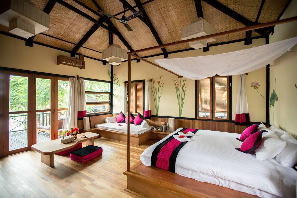 Une pièce spacieuse avec un grand lit, un lit plus petit et un canapé-lit. Elle dispose d’un balcon avec une terrasse en bois et une vue sur la verdure.