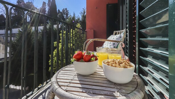 Ein Balkon mit einem Tisch, gedeckt für das Frühstück, einschließlich einer Schale Erdbeeren, einem Glas Orangensaft und einer Schale Granola.