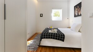 Ein modernes Schlafzimmer mit Bett, Fenster, Nachttisch und einem Wandbild.