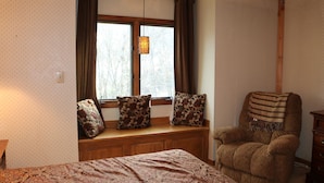 Une pièce comprenant un lit, un siège de fenêtre agrémenté de coussins à motifs, une chaise en bois et un luminaire suspendu.
