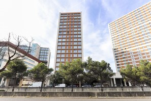 A tall, modern building with a grid of windows, surrounded by trees and a concrete barrier. - Expo Panoramic View by Homing (Lisbon)