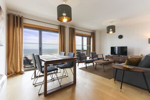 A modern living room with a dining area, large windows, a flat-screen TV, and a view of the sea. - Expo Panoramic View by Homing (Lisbon)