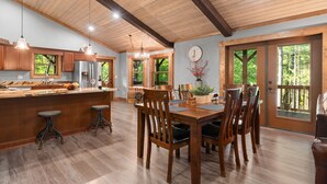 A spacious kitchen with wooden cabinets, a large island with stools, and a dining area with wooden chairs. - 2019 Newly Built ~ LUXURY Cabin ~ 23 Acre Estate ~ Hot Tub ~ 8 miles to Downtown (Asheville)