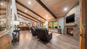 A spacious living room with a fireplace, leather recliners, a flat-screen TV, and a kitchen area in the background. - 2019 Newly Built ~ LUXURY Cabin ~ 23 Acre Estate ~ Hot Tub ~ 8 miles to Downtown (Asheville)