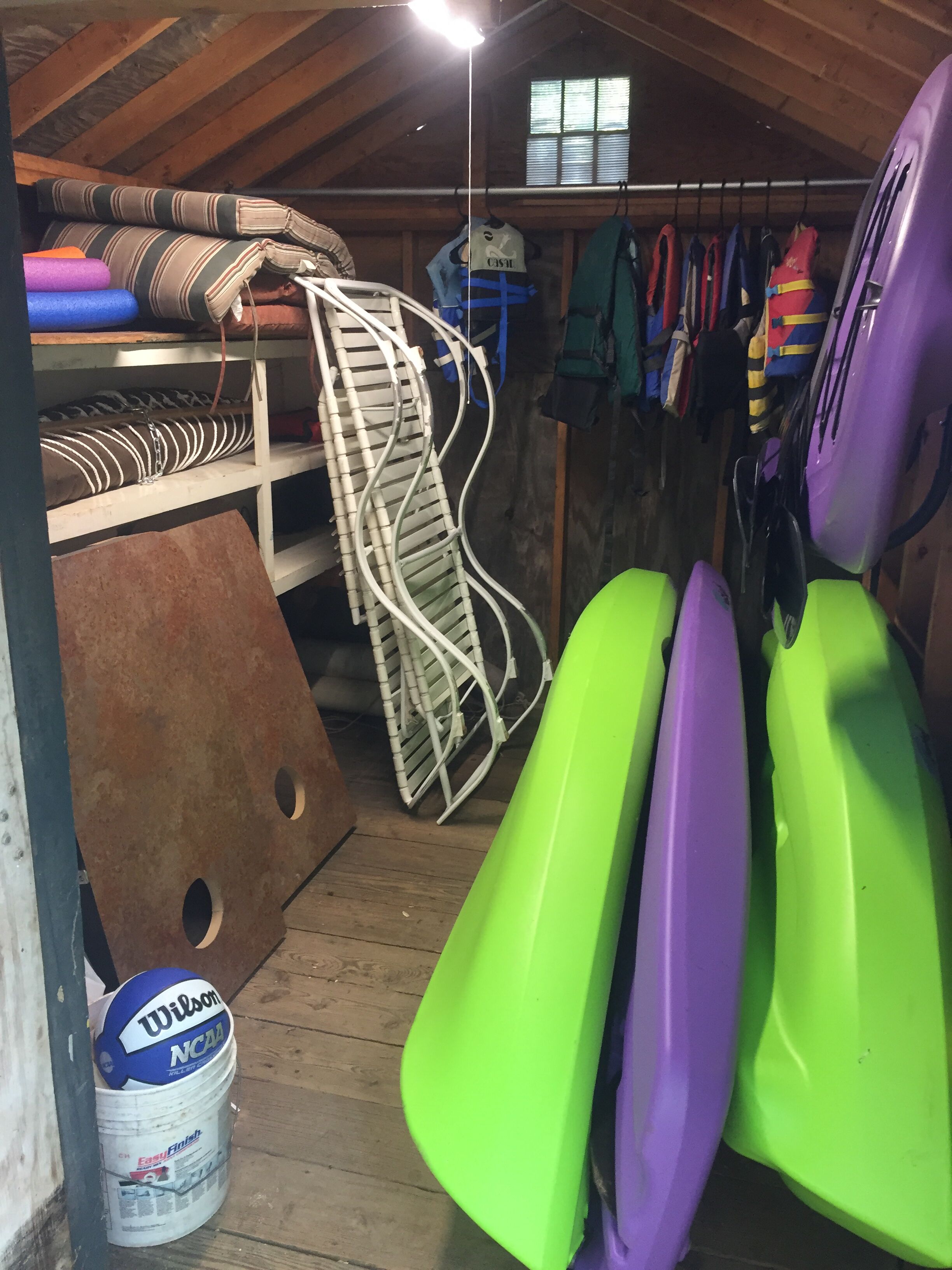 A storage area with various items including a bucket labeled "Wilson NCAA," a metal rack, and several colorful jackets hanging on a line.