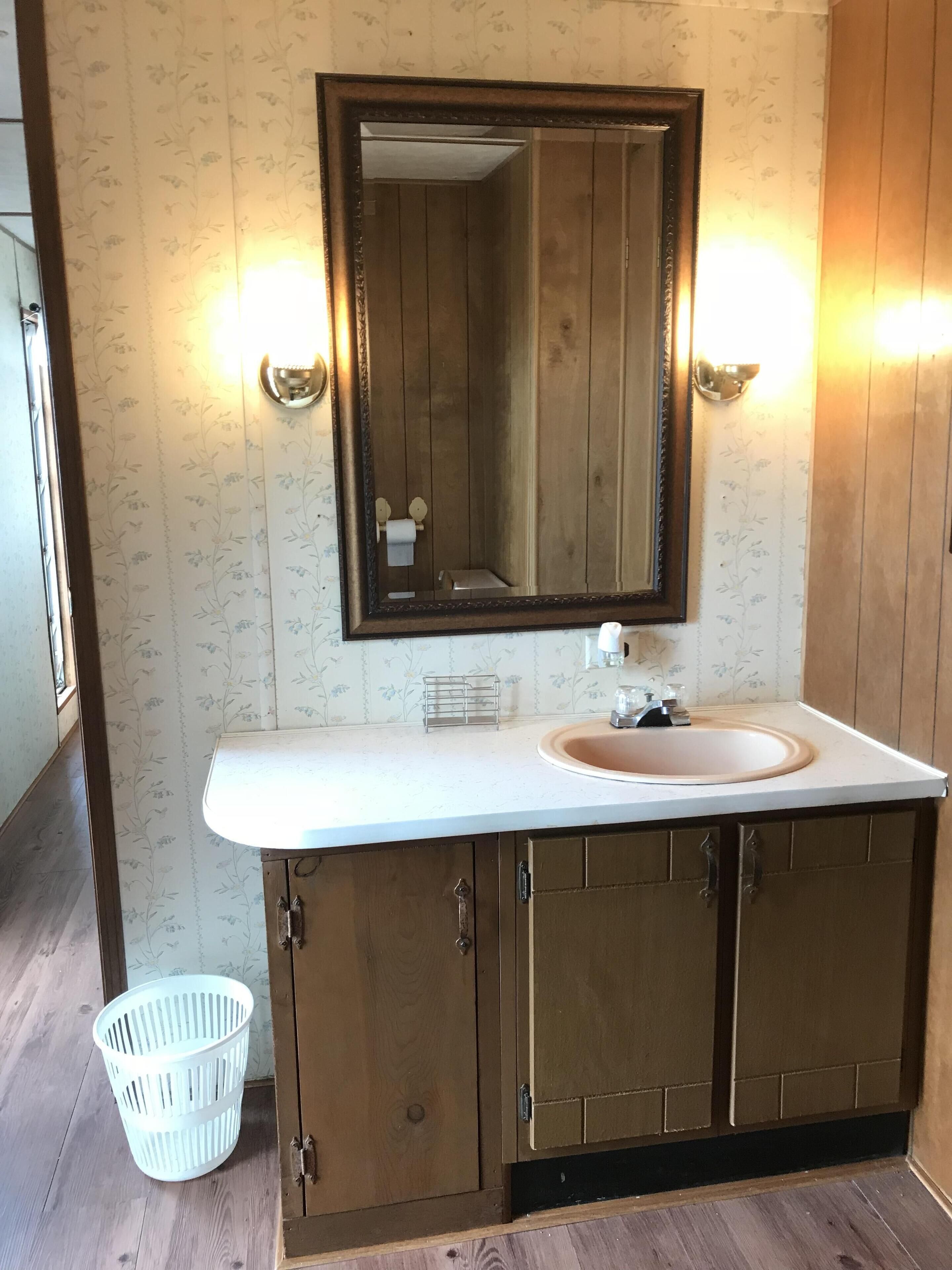 Ein Badezimmer mit einem Holzlagerflächenmöbel, einem großen Spiegel und einem Waschbecken.