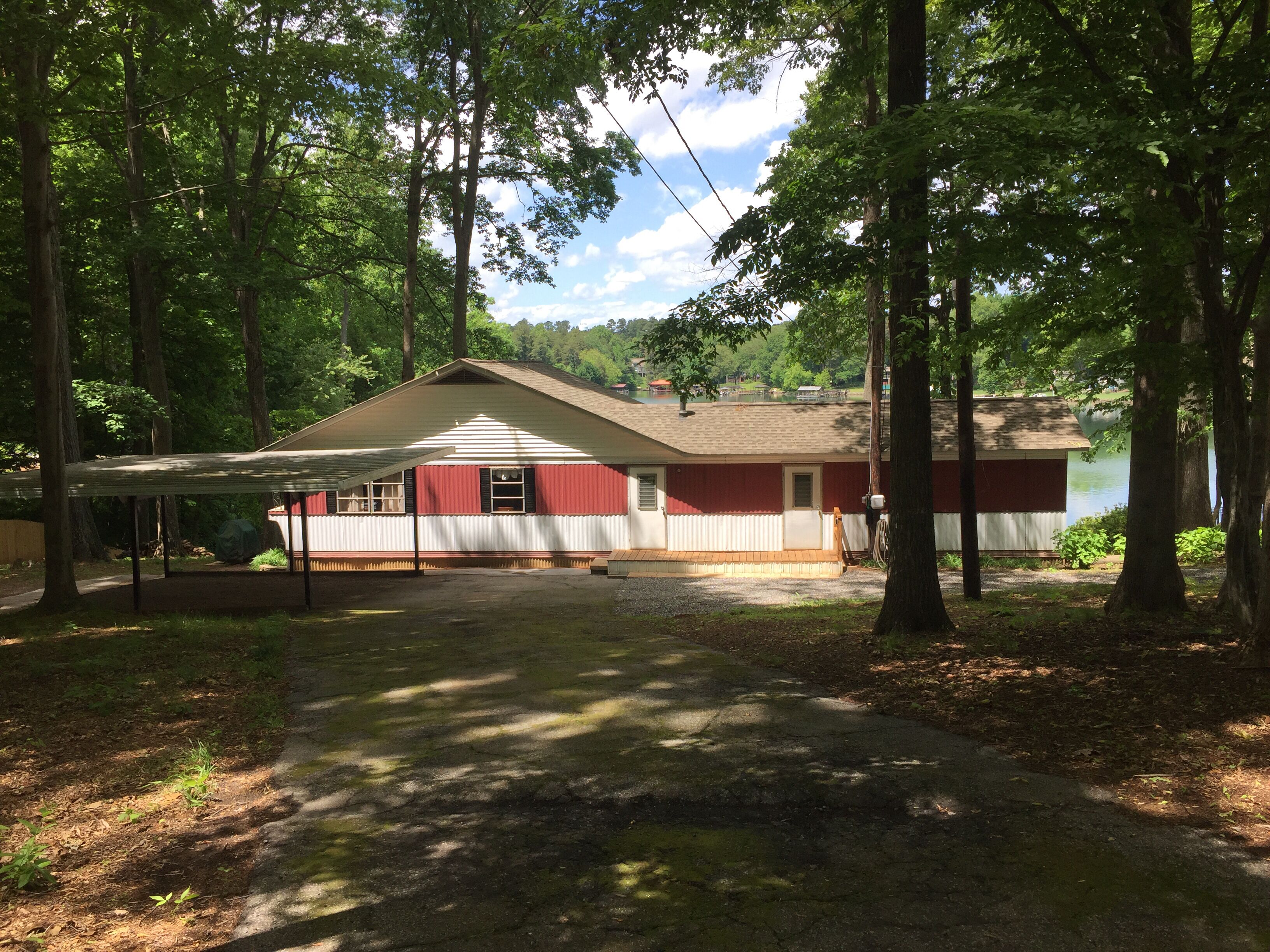 A single-story house with a red and white exterior, surrounded by trees and a lake.