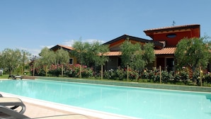 A swimming pool with a tiled deck, surrounded by lush greenery and flowering plants. - Locanda dei Rii (Manerba del Garda)