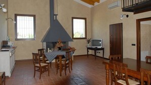 A spacious dining area with a large table and chairs, a kitchen area with a stove, and a TV on a small table. - Locanda dei Rii (Manerba del Garda)