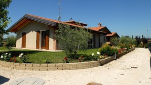 A two-story house with a red-tiled roof, a brick foundation, and a well-maintained garden with various plants and flowers. - Locanda dei Rii (Manerba del Garda)