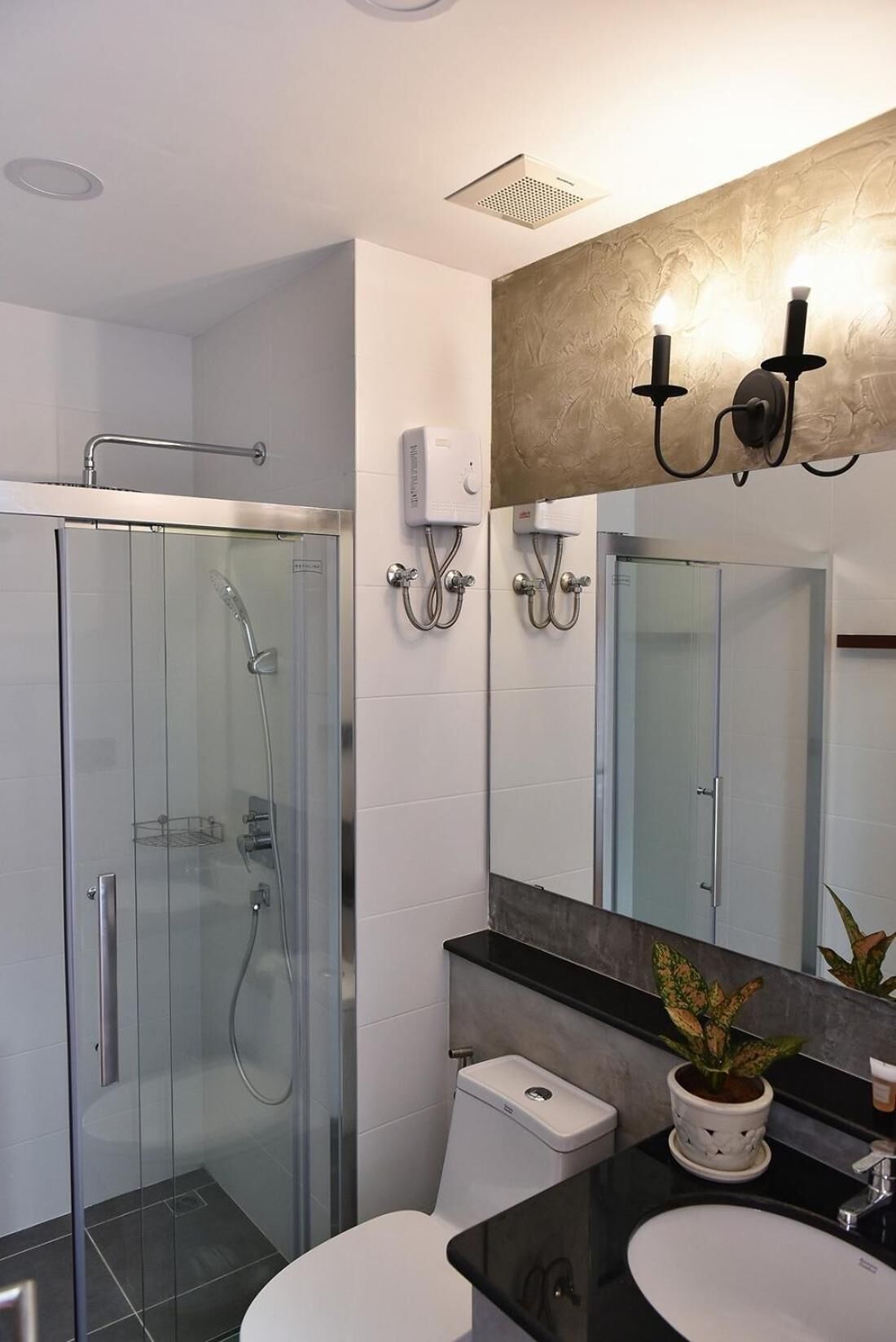 Une salle de bain moderne dotée d’une douche à parois de verre, de toilettes, d’un lavabo et d’un miroir avec un luminaire fixé au mur.