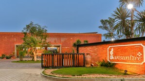 Un bâtiment moderne à la façade en briques rouges, doté d’une pelouse bien entretenue et d’une enseigne indiquant le nom « Sansuntree ».