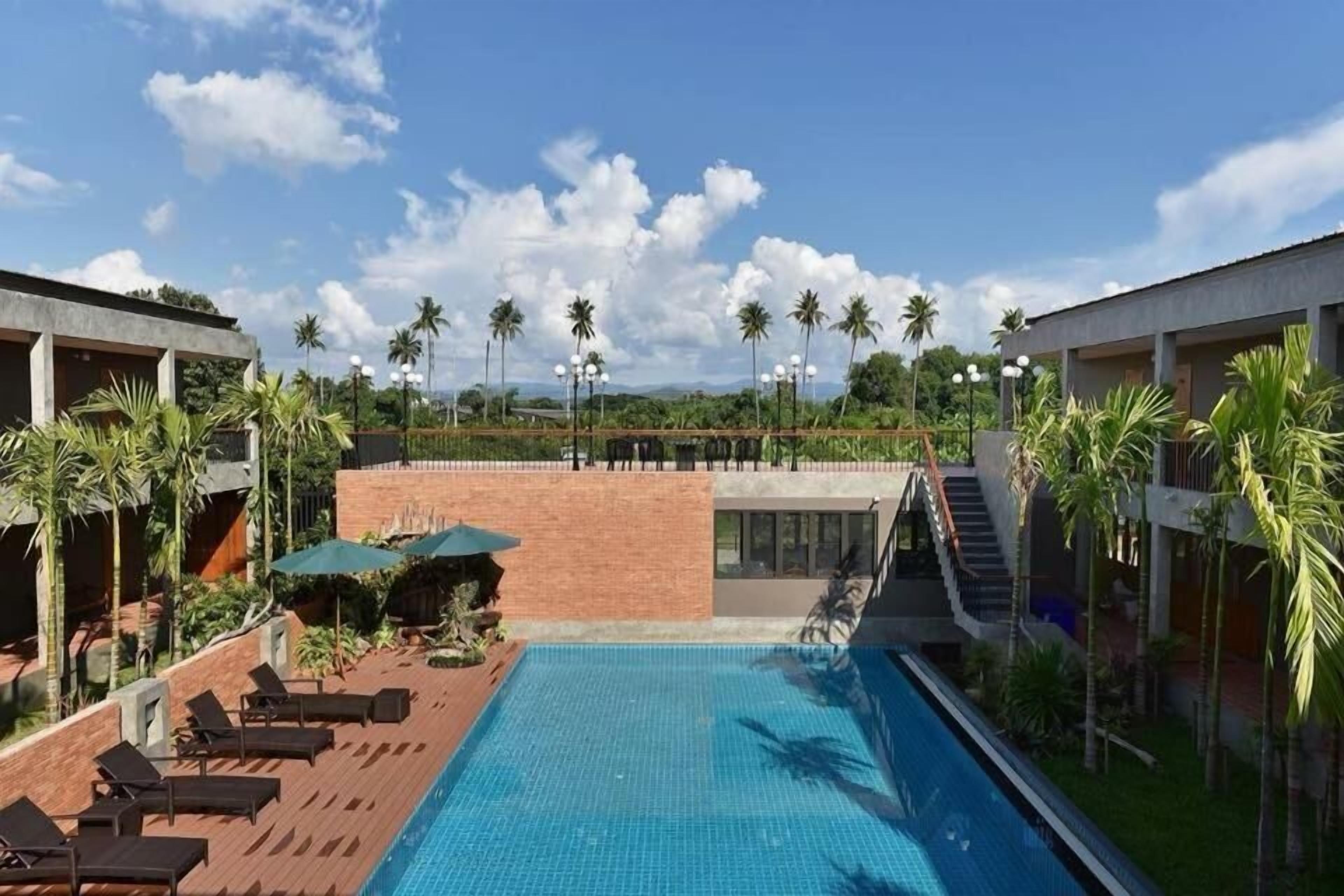 A swimming pool with lounge chairs, palm trees, and a clear sky.