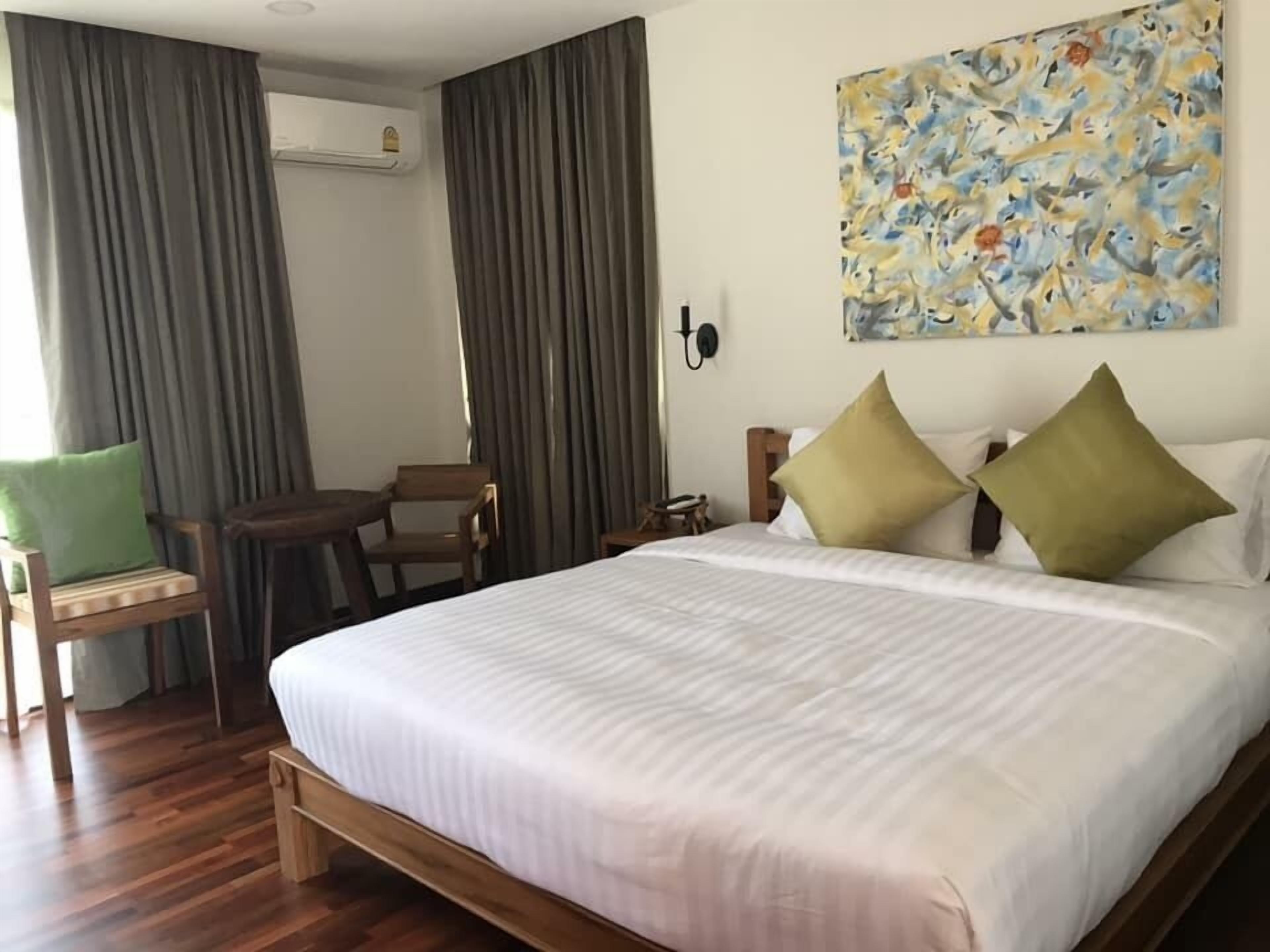 A hotel room with a large bed, a small table, two chairs, a painting on the wall, and a window with curtains.