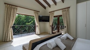 A bedroom with a bed, curtains, a TV, and a balcony with a view of trees. - San Lameer Villa Rentals 403 (Southbroom)