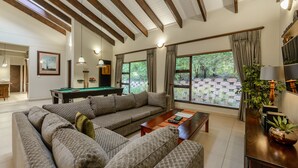 A modern living room with a sectional sofa, a pool table, and large windows offering a view of the outdoors. - San Lameer Villa Rentals 403 (Southbroom)