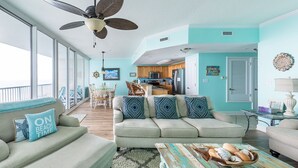 Un vaste espace de vie comprenant un grand canapé, une table basse et un ventilateur de plafond. Il y a également une cuisine avec des meubles en bois et une table à manger.