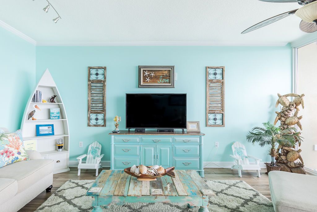 A living room with a teal wall, a white bookshelf, a flat-screen TV, and a decorative turtle statue.
