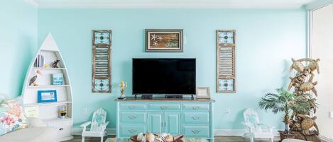A living room with a teal wall, a white bookshelf, a flat-screen TV, and a decorative turtle statue.