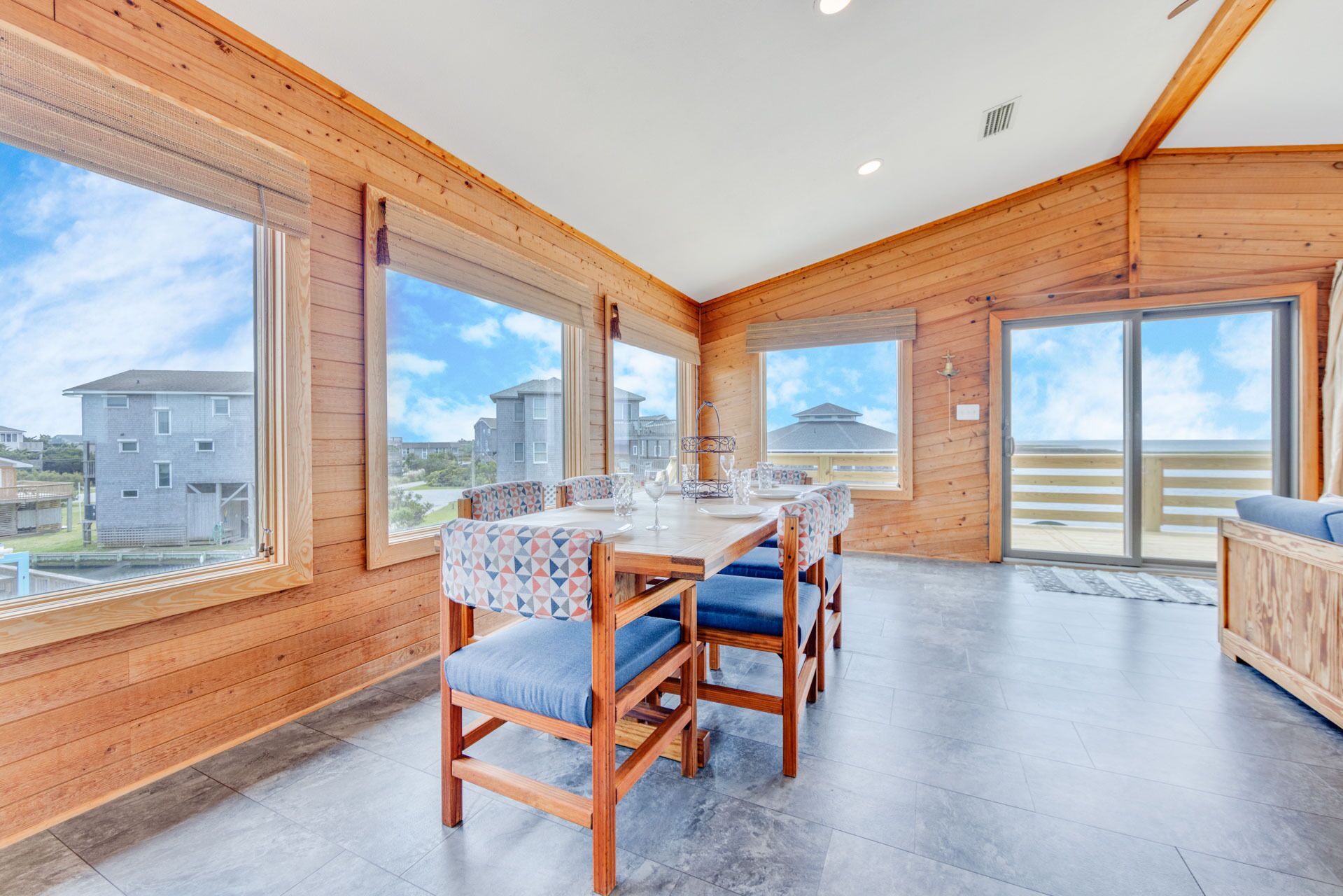 A wooden interior with a dining area, large windows, and a view of buildings outside.