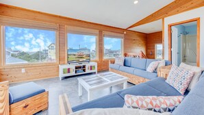 Ein geräumiges Wohnzimmer mit Holzwänden, einem großen Fernseher und einem Sofa mit gemusterten Kissen.