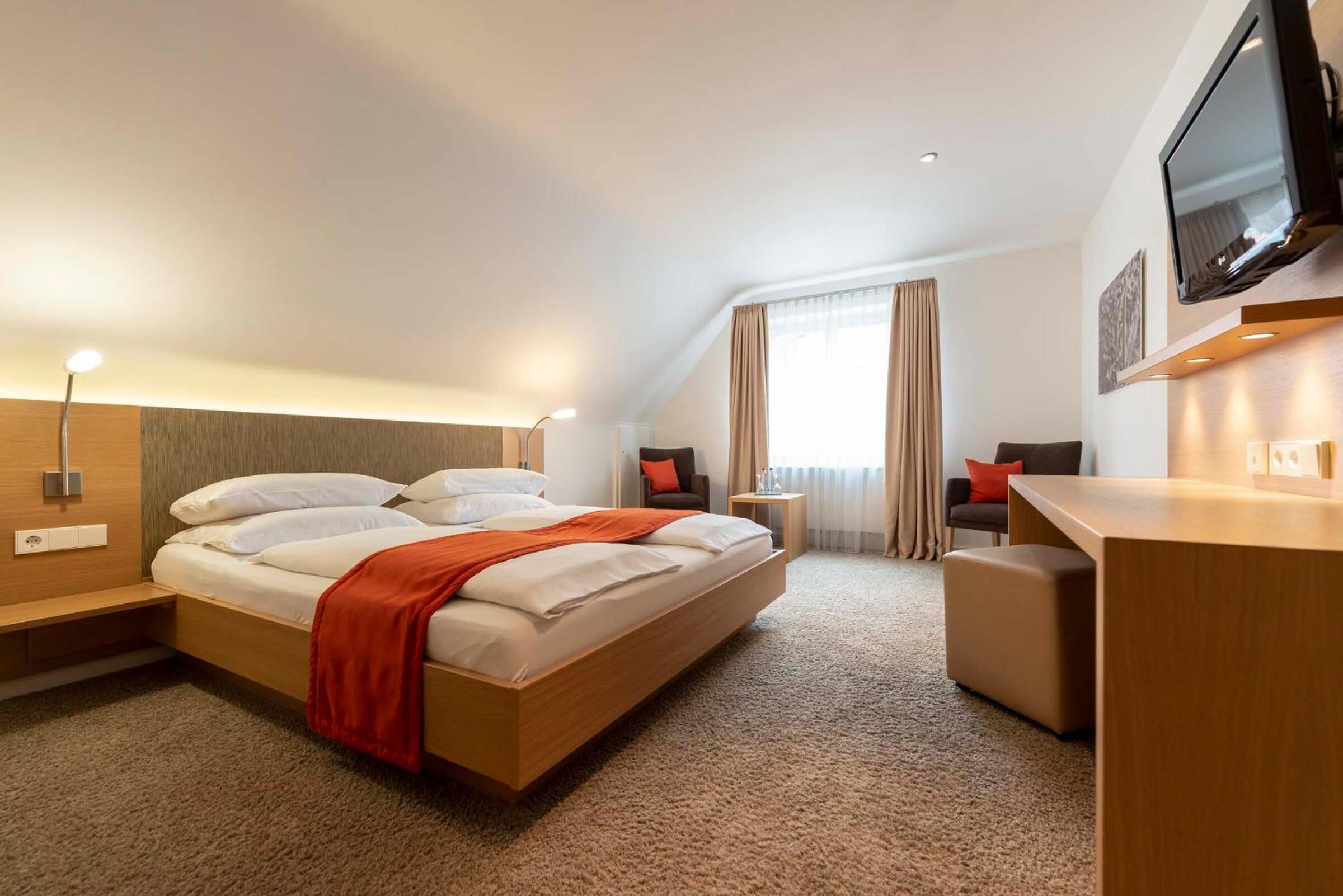 A hotel room with a bed, a desk, a chair, a TV, and a window with curtains.