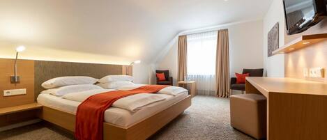 A hotel room with a bed, a desk, a chair, a TV, and a window with curtains.