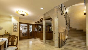 A spacious lobby with a checkered floor, a reception desk, a staircase, and a decorative ceiling light. - Hotel Gasthof Krone (Niederstetten)
