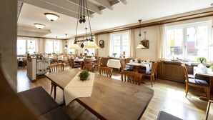 A spacious dining area with wooden tables and chairs, pendant lighting, and large windows providing natural light. - Hotel Gasthof Krone (Niederstetten)