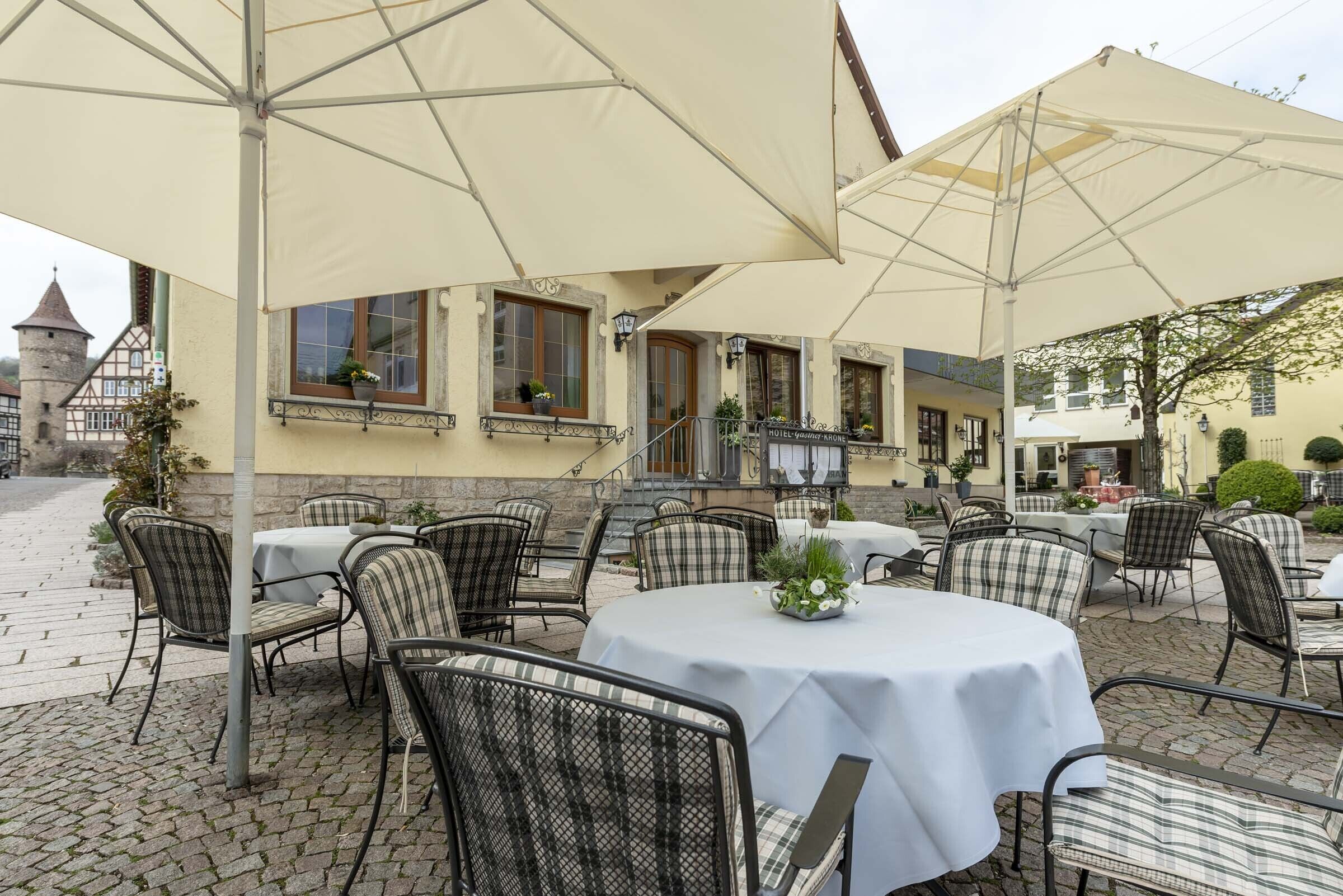 An outdoor seating area with tables and chairs, covered by large umbrellas, and a building with a sign reading "HOTEL VINEYARD-TRINITY".