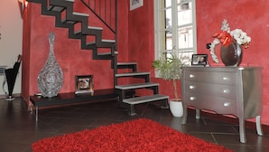 A staircase with a red wall, a potted plant, a vase with flowers, and a dresser with drawers. - Luxury apartment located 500 metres from  historic centre and railway station (Varese)