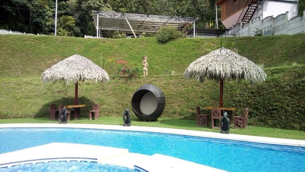 A swimming pool with two thatched umbrellas, a tire sculpture, and a statue of a man. - beuatifull house in the mountains with beach view (Savegre)