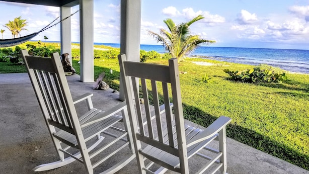 Two rocking chairs on a covered porch with a view of the ocean.