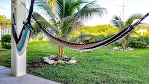 A hammock tied between two concrete pillars in a garden with palm trees and a clear sky.