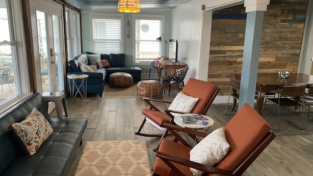 A cozy living room with a sofa, ottomans, and a coffee table. There is a dining area with a table and chairs.