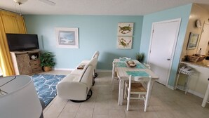 A living room with a TV, a sofa, a dining table with chairs, and a kitchen area.