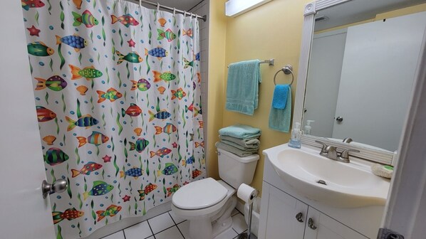 Un baño con inodoro blanco, lavabo con espejo y cortina de ducha con estampado de peces.
