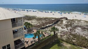 A beachfront hotel with a pool, beach umbrellas, and a wooden boardwalk leading to the beach.