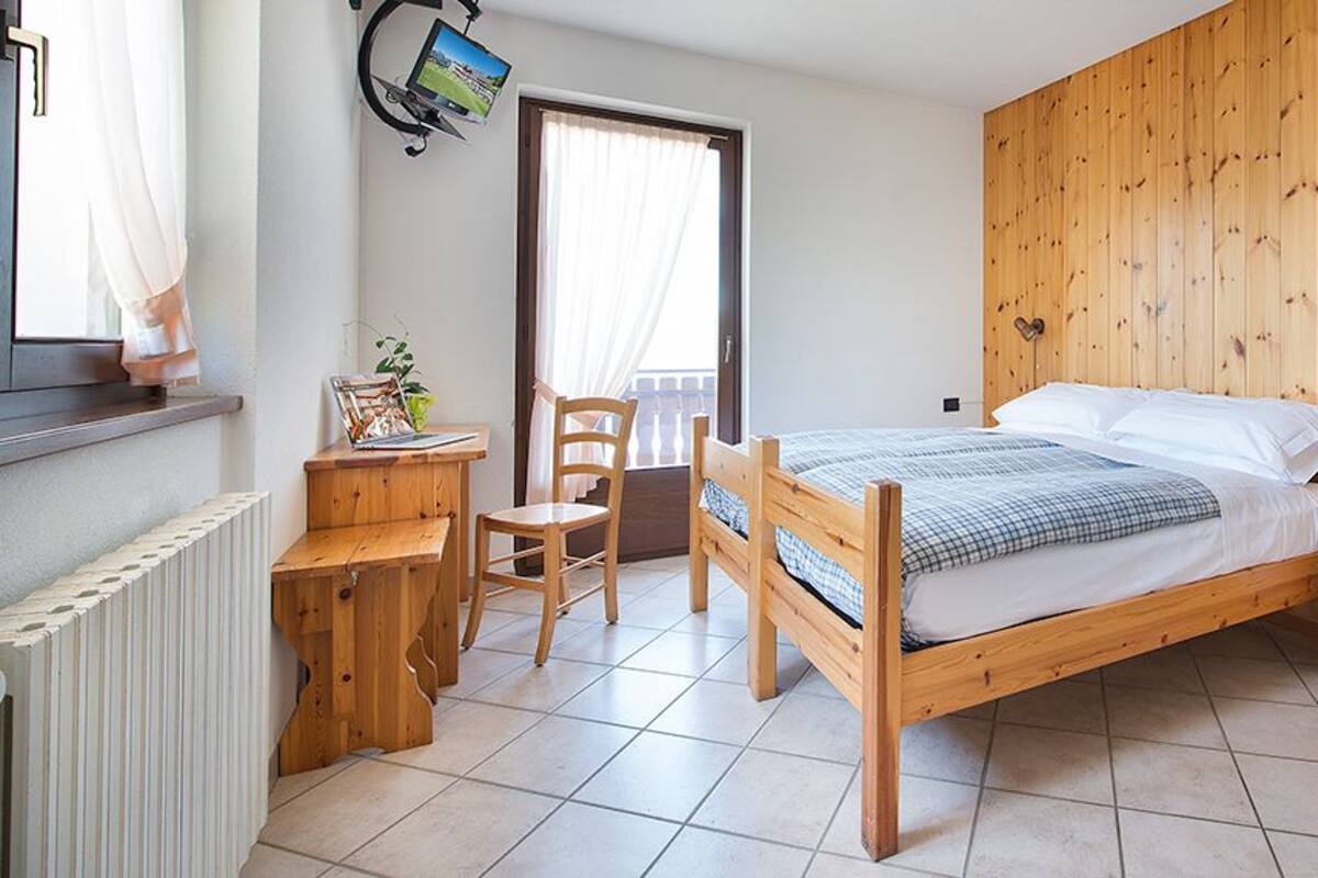 A bedroom with a wooden bed, a desk, a chair, and a radiator.