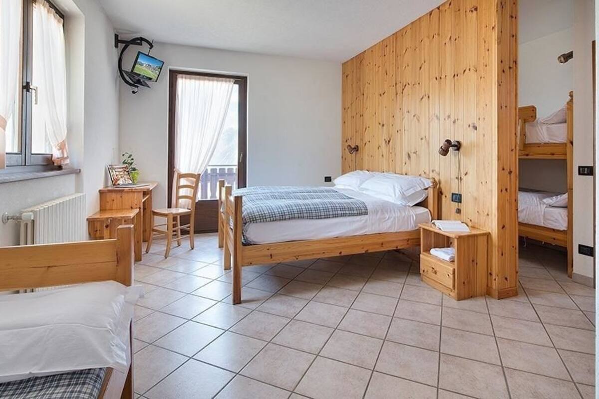 A bedroom with a wooden bed, a desk, a chair, and a TV mounted on the wall.
