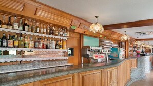 Zona de bar con estantes de madera llenos de botellas, una máquina de café y una caja registradora.