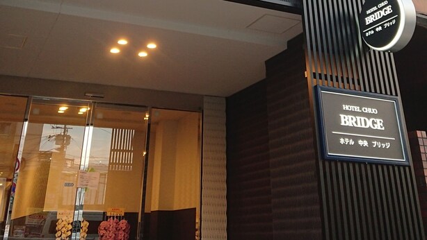 A hotel entrance with a modern facade, a signboard, and a glass door with flowers. - Hotel Chuo Bridge (Osaka)