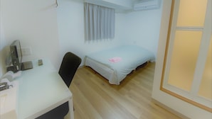 A small, clean room with a bed, a desk with a chair, a window with curtains, and an air conditioning unit on the wall. - Hotel Chuo Bridge (Osaka)